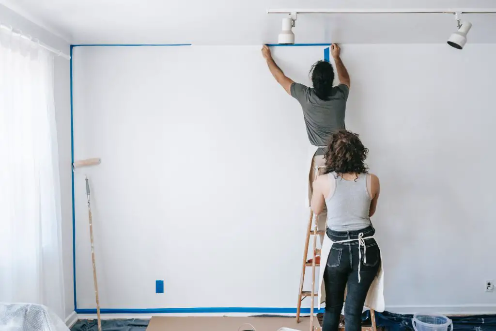 People taping edges of a wall in a room