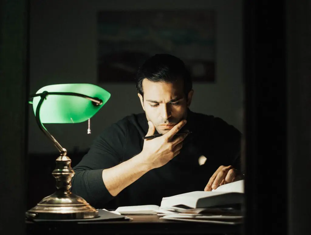 Man holding pen while reading with lamp