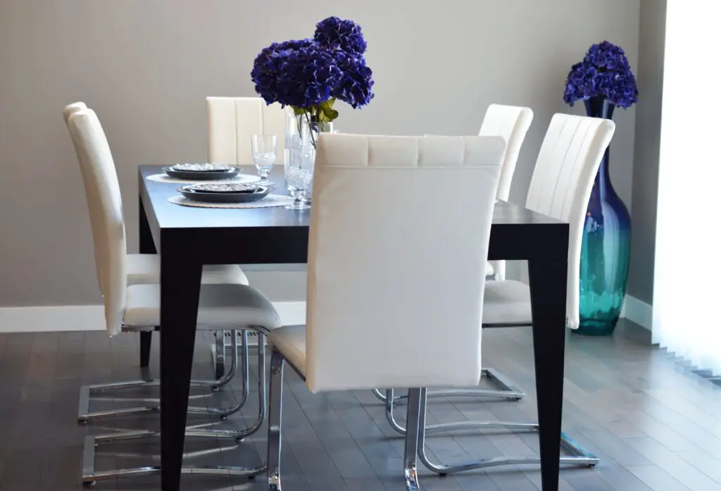 A dinner table with white chairs and purple flowers