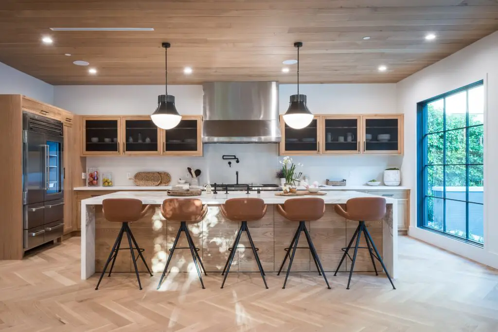 A brown toned kitchen area with chairs, cabinets and lights