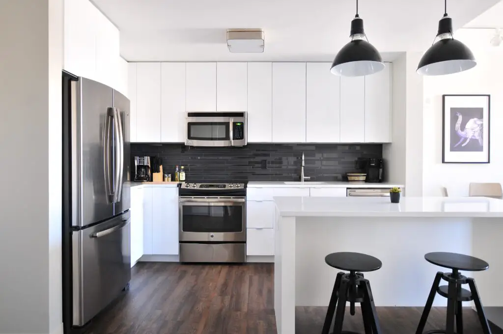 A black and white toned kitchen area with chairs, cabinets and lights