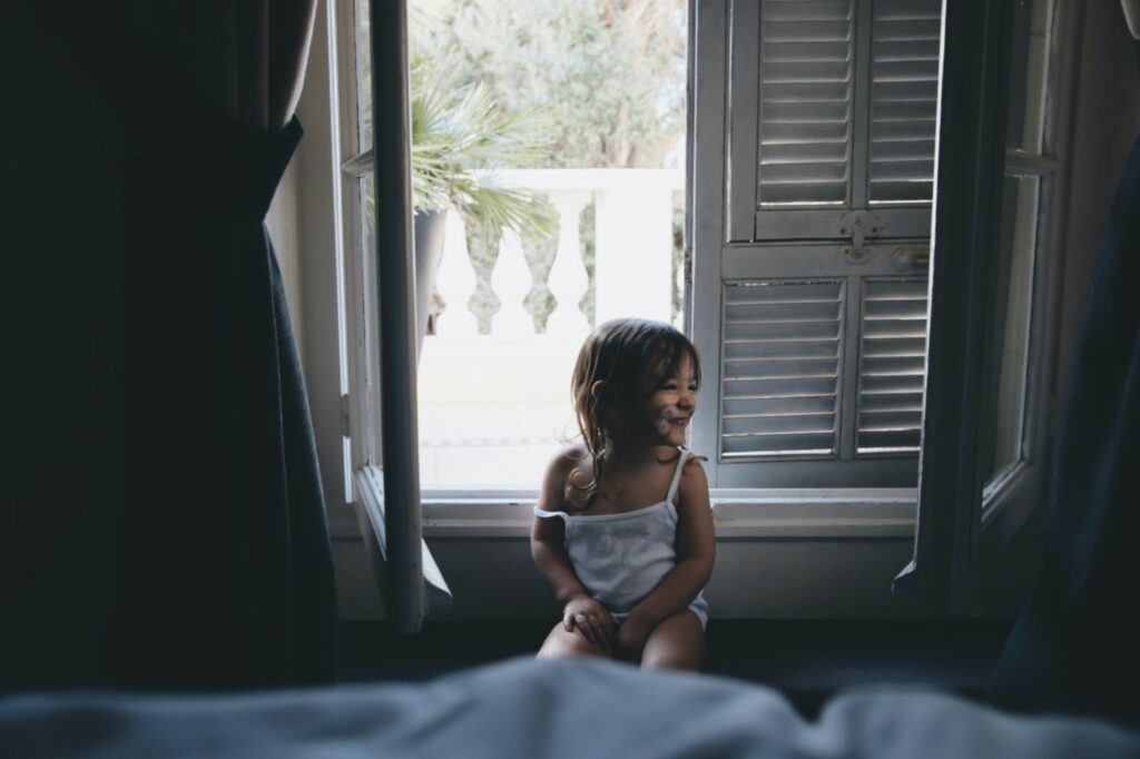 A baby girl sitting beside an open window