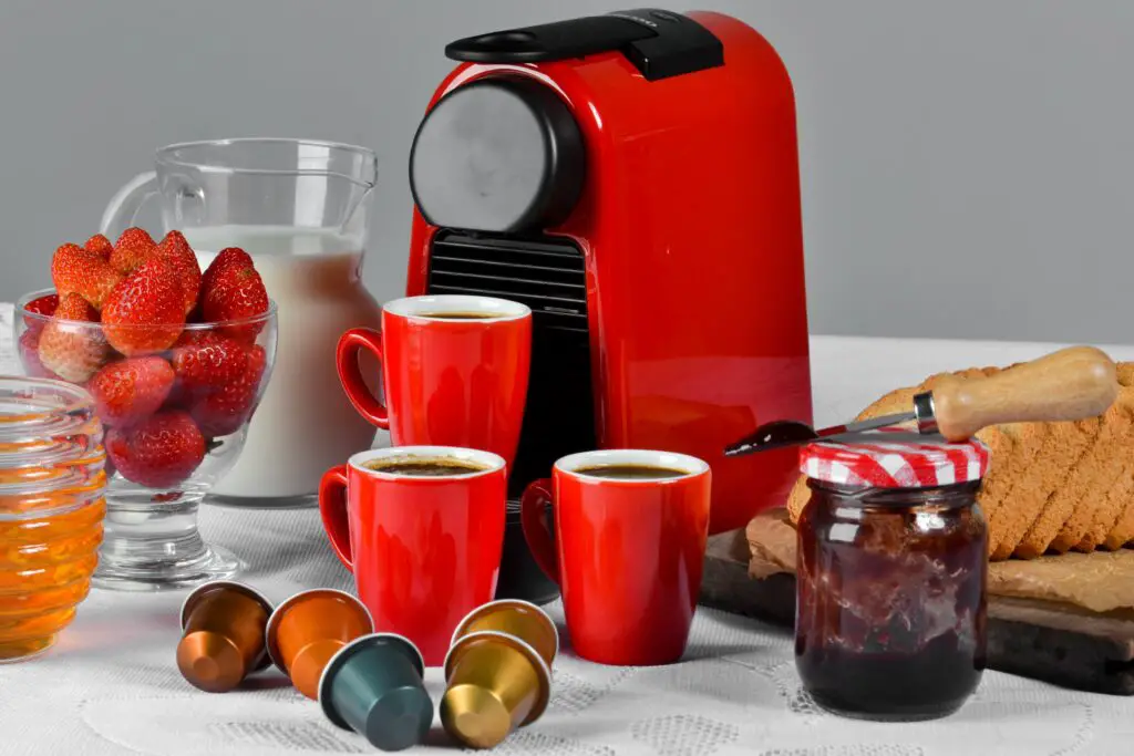 A red coffee maker with red mugs filled with coffee