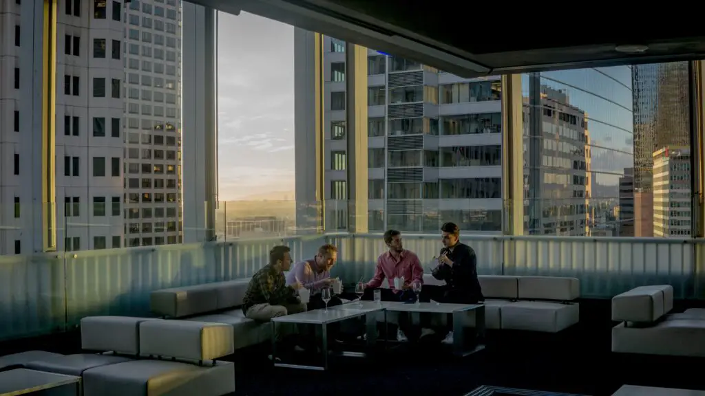 People eating and drinking while sitting on a sectional sofa near the window