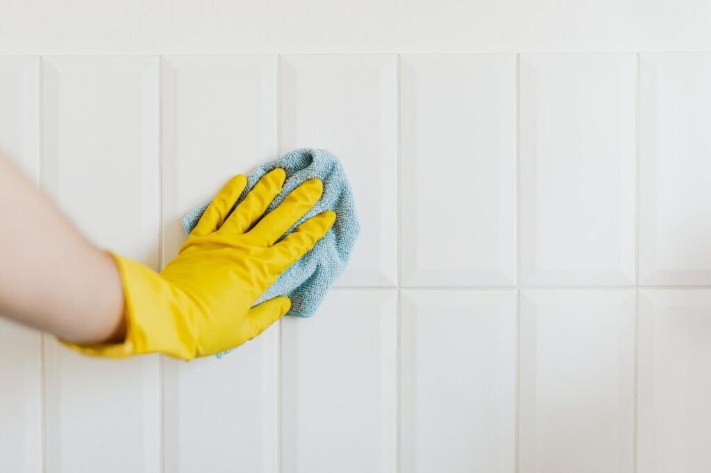 A person wearing yellow gloves cleaning a white wall