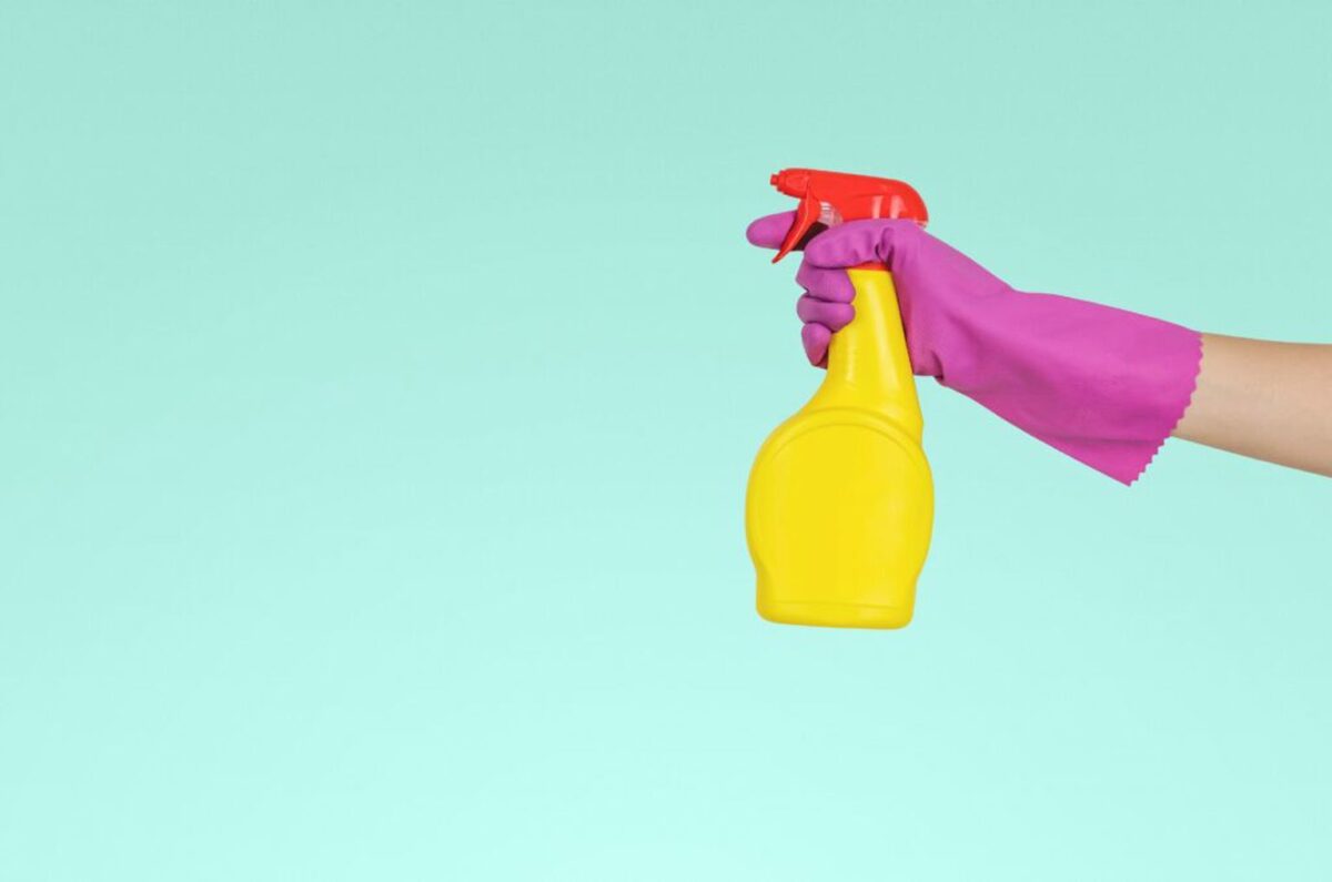 Pink gloved hands holding a yellow bottle spray cleaner with a red nozzle
