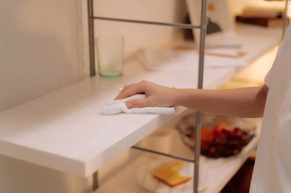 White rag being used by a person to clean the white colored kitchen cabinet display area